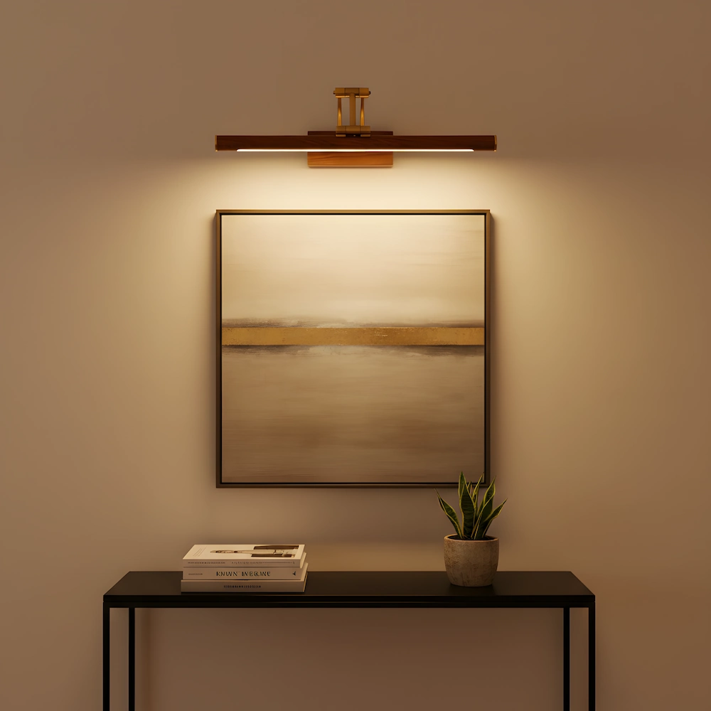 Brass picture light with wood base illuminating abstract landscape painting above black console table with warm LED glow